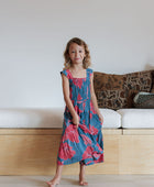 Girl wearing long blue sleeveless dress with large red and pink floral print.