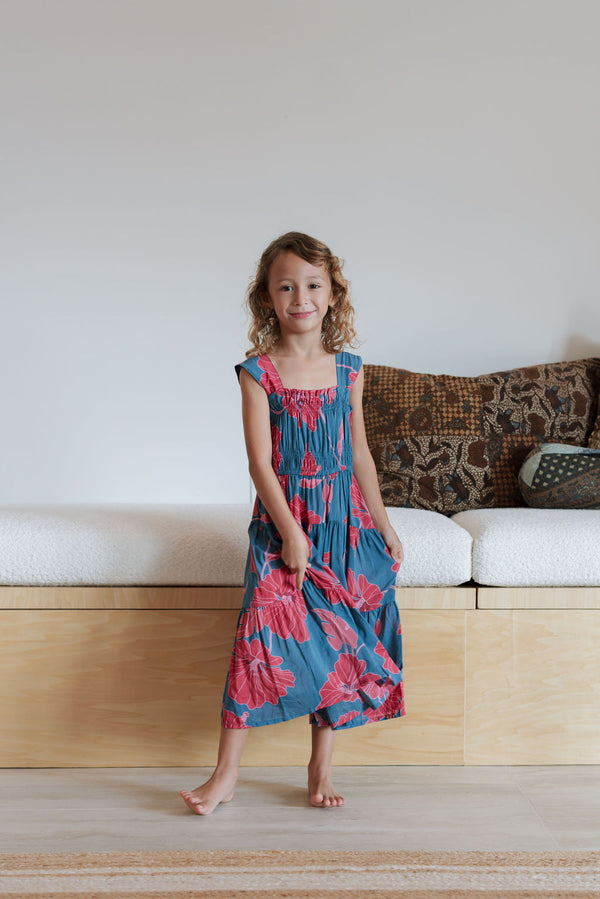 Girl wearing long blue sleeveless dress with large red and pink floral print.