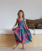 Girl wearing long blue sleeveless dress with large red and pink floral print.