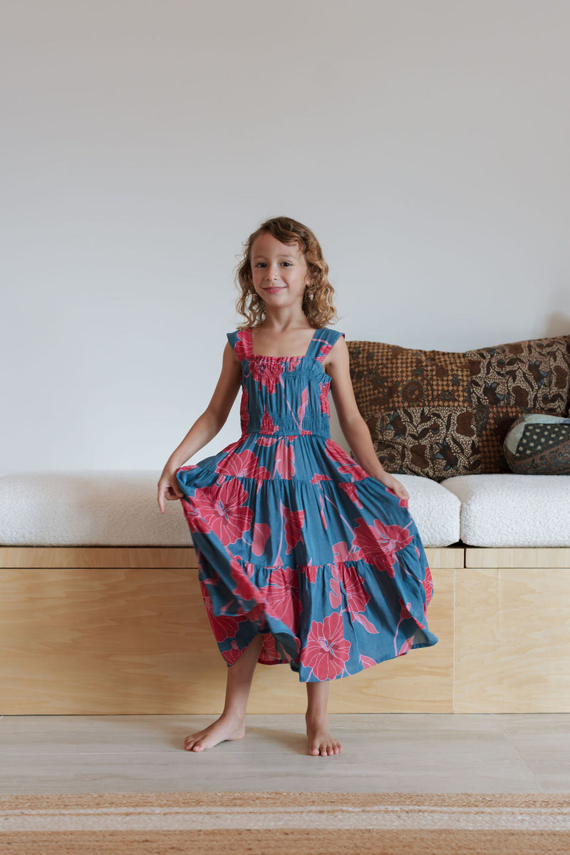 Girl wearing long blue sleeveless dress with large red and pink floral print.