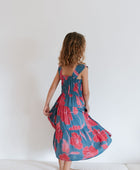 Girl wearing long blue sleeveless dress with large red and pink floral print.