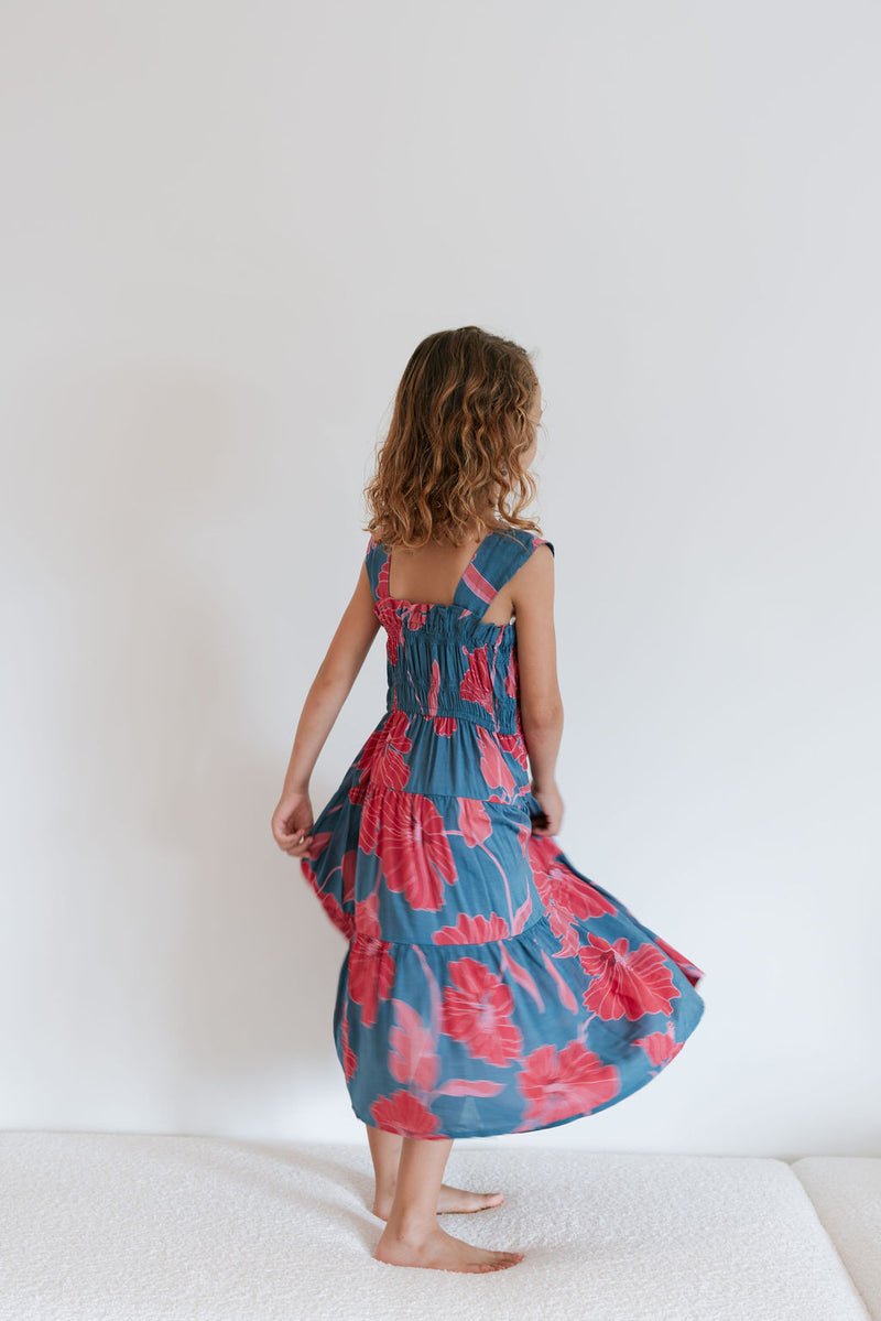 Girl wearing long blue sleeveless dress with large red and pink floral print.