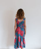 Girl wearing long blue sleeveless dress with large red and pink floral print.