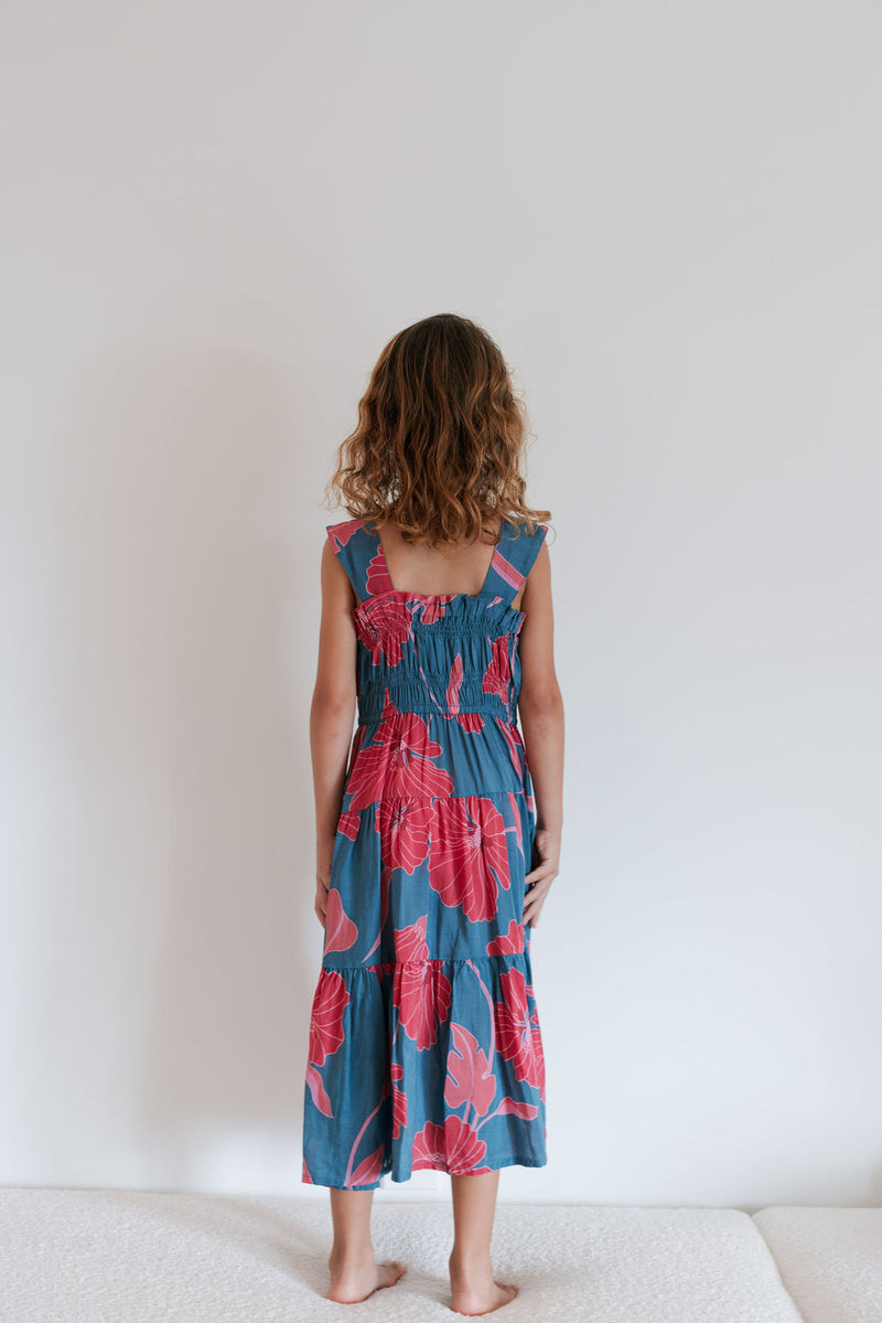 Girl wearing long blue sleeveless dress with large red and pink floral print.