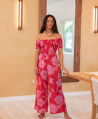 Woman wearing long red off shoulder jumpsuit with large pink floral print.