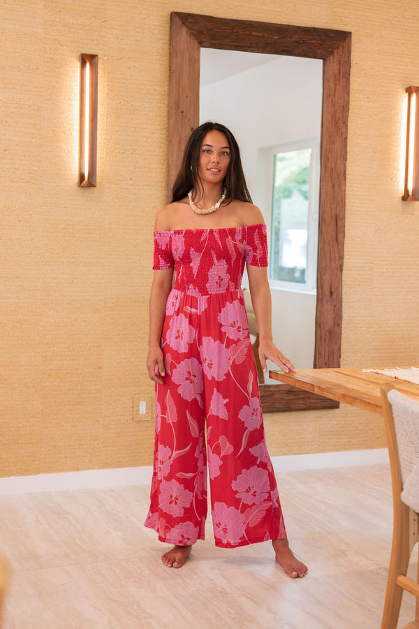 Woman wearing long red off shoulder jumpsuit with large pink floral print.