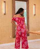 Woman wearing long red off shoulder jumpsuit with large pink floral print.