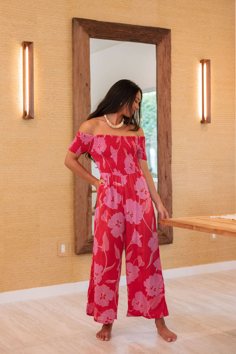 Woman wearing long red off shoulder jumpsuit with large pink floral print.