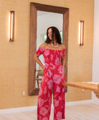 Woman wearing long red off shoulder jumpsuit with large pink floral print.