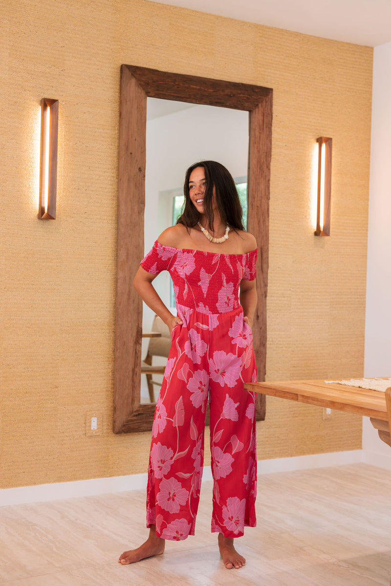 Woman wearing long red off shoulder jumpsuit with large pink floral print.