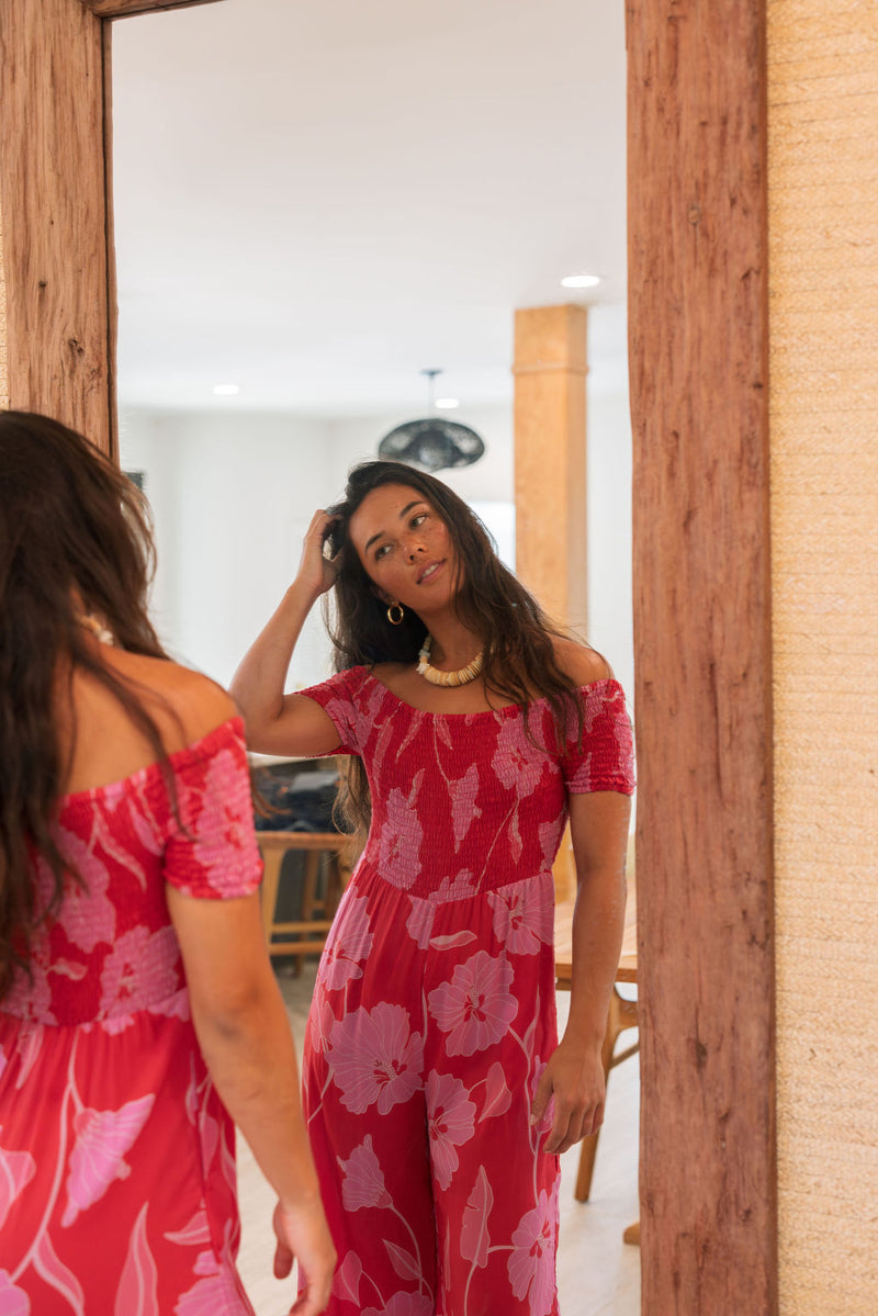 Woman wearing long red off shoulder jumpsuit with large pink floral print.