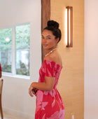 Woman wearing long red off shoulder jumpsuit with large pink floral print.