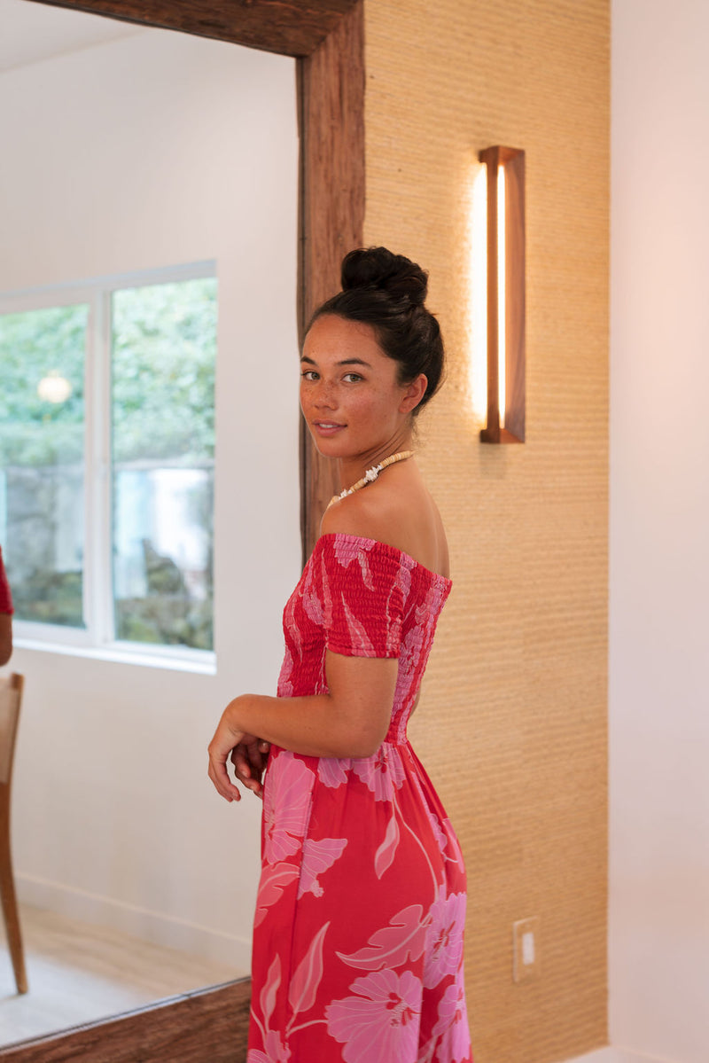 Woman wearing long red off shoulder jumpsuit with large pink floral print.