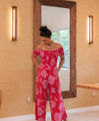 Woman wearing long red off shoulder jumpsuit with large pink floral print.