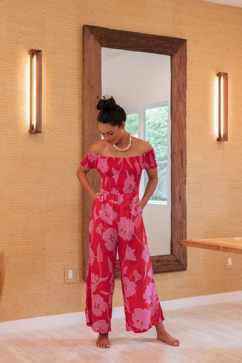 Woman wearing long red off shoulder jumpsuit with large pink floral print.