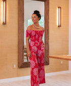 Woman wearing long red off shoulder jumpsuit with large pink floral print.