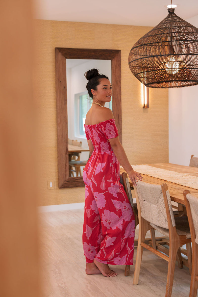 Woman wearing long red off shoulder jumpsuit with large pink floral print.