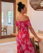 Woman wearing long red off shoulder jumpsuit with large pink floral print.