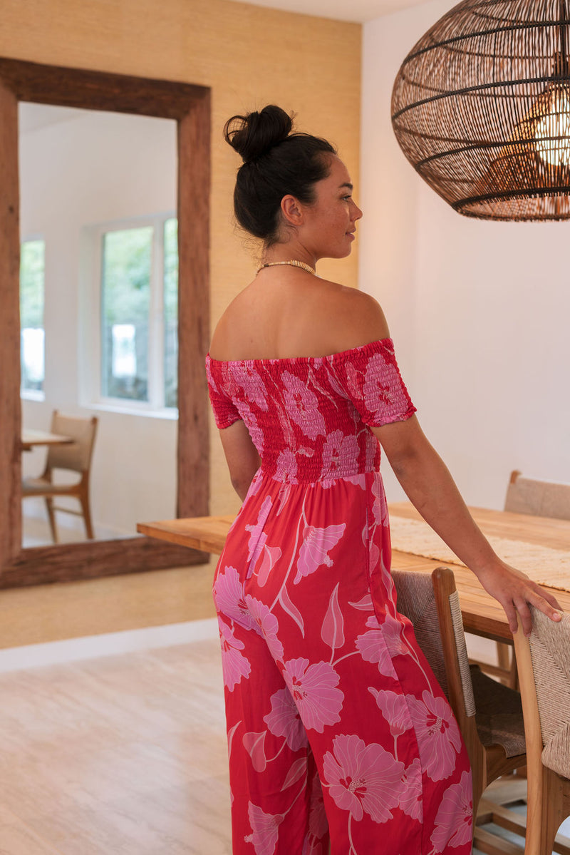 Woman wearing long red off shoulder jumpsuit with large pink floral print.