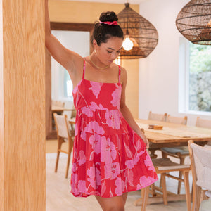 Woman wearing short red sleeveless dress with large pink floral print.
