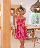 Woman wearing short red sleeveless dress with large pink floral print.