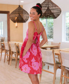 Woman wearing short red sleeveless dress with large pink floral print.