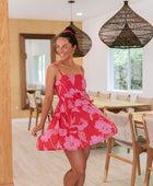 Woman wearing short red sleeveless dress with large pink floral print.