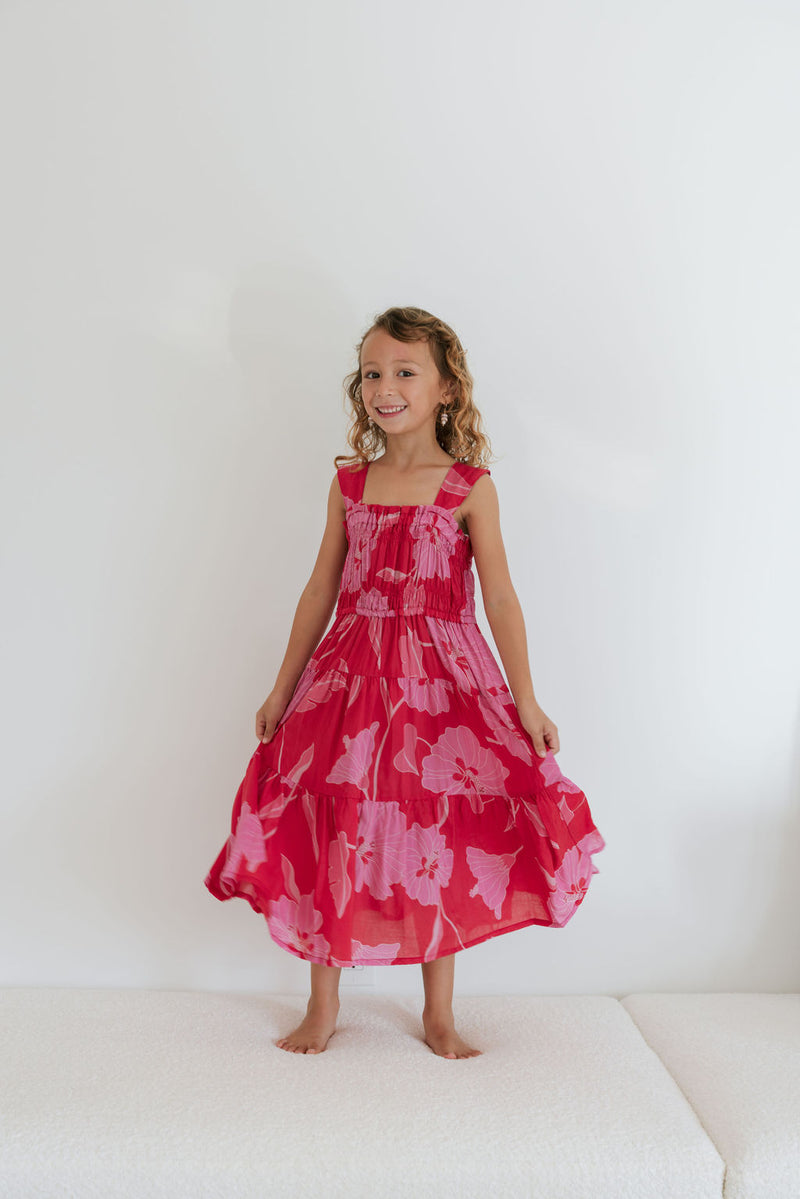 Girl wearing long red sleeveless dress with large pink floral print.