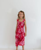 Girl wearing long red sleeveless dress with large pink floral print.