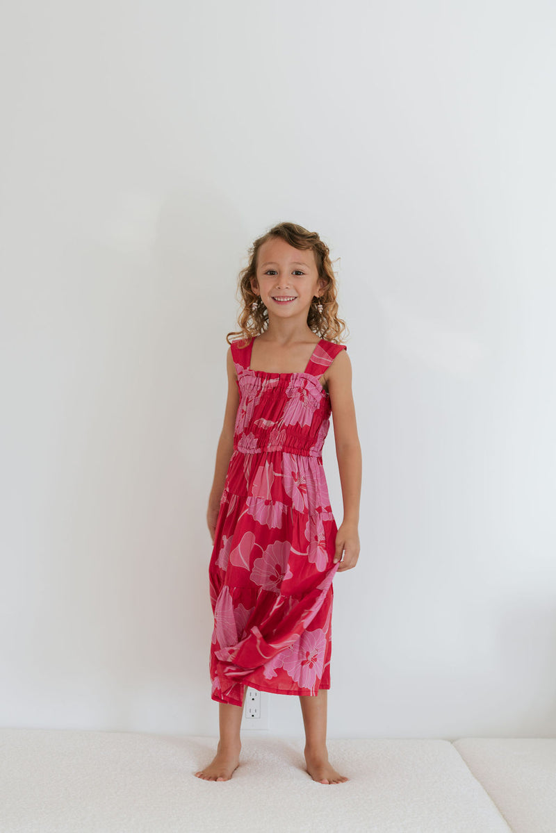 Girl wearing long red sleeveless dress with large pink floral print.