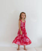 Girl wearing long red sleeveless dress with large pink floral print.