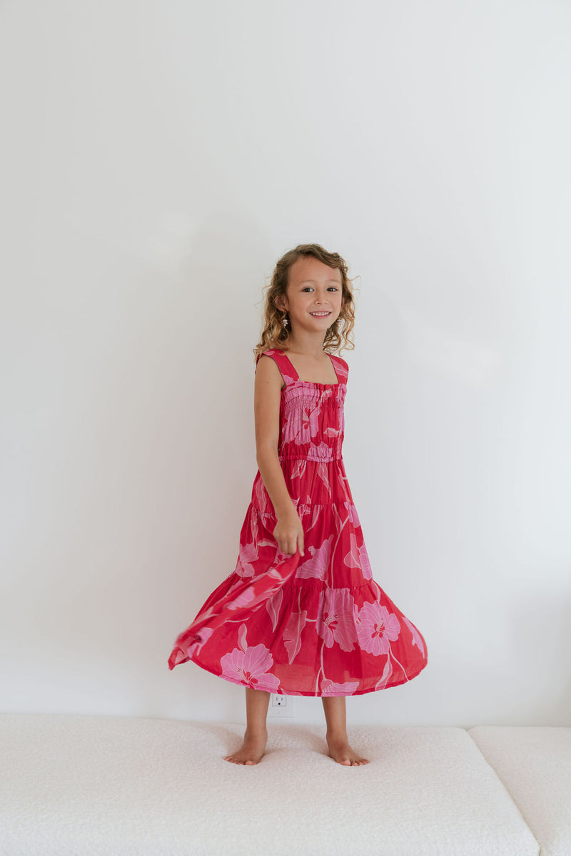 Girl wearing long red sleeveless dress with large pink floral print.