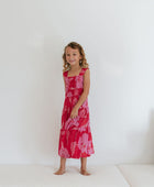 Girl wearing long red sleeveless dress with large pink floral print.