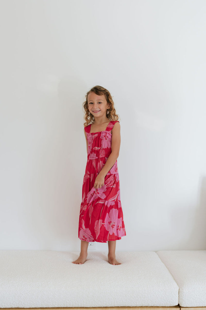 Girl wearing long red sleeveless dress with large pink floral print.