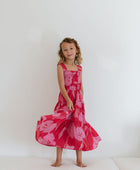 Girl wearing long red sleeveless dress with large pink floral print.