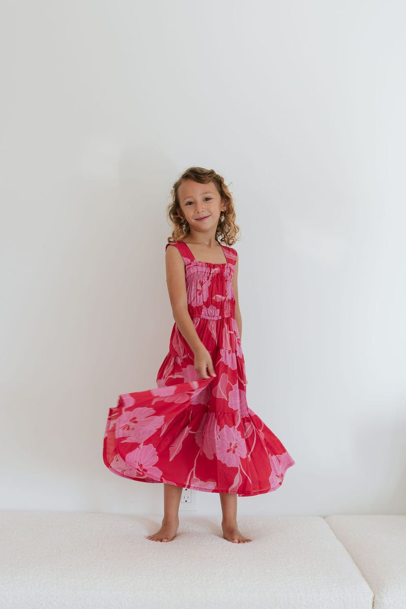 Girl wearing long red sleeveless dress with large pink floral print.