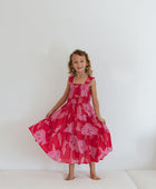 Girl wearing long red sleeveless dress with large pink floral print.