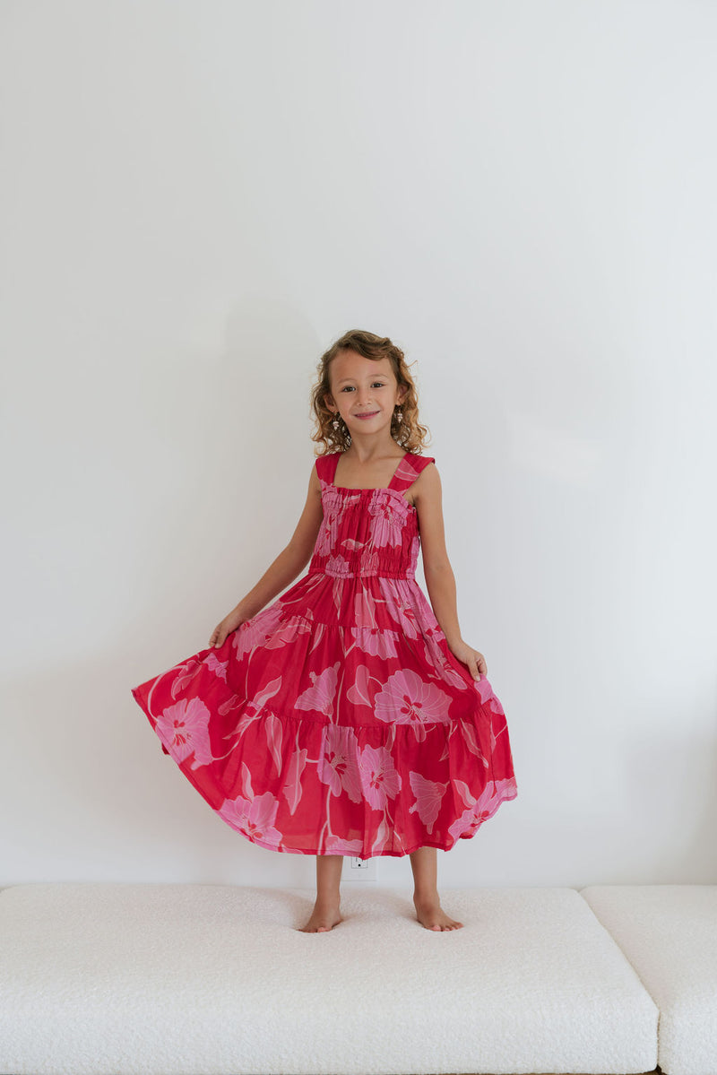 Girl wearing long red sleeveless dress with large pink floral print.