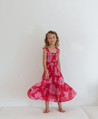 Girl wearing long red sleeveless dress with large pink floral print.