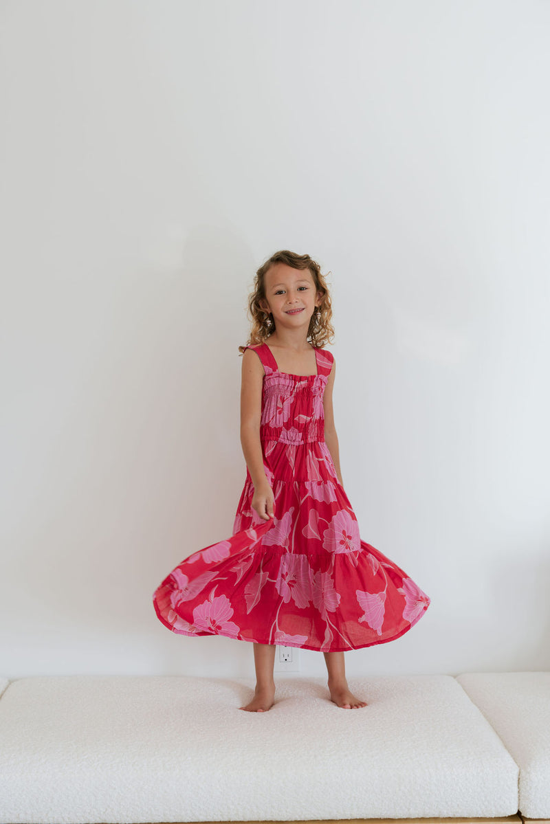 Girl wearing long red sleeveless dress with large pink floral print.