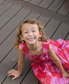 Girl wearing long red sleeveless dress with large pink floral print.