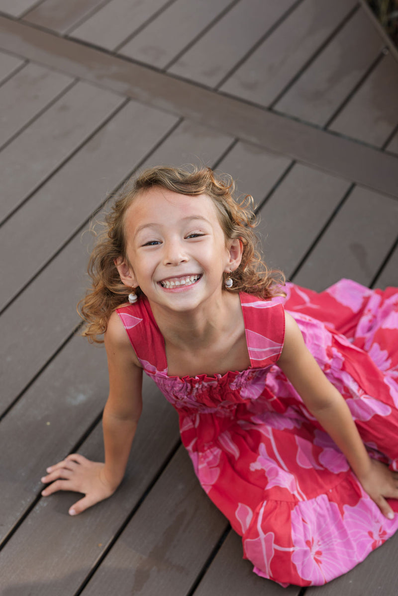 Girl wearing long red sleeveless dress with large pink floral print.