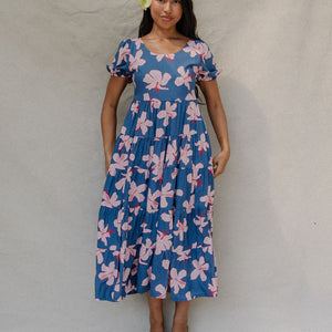 woman with brown hair wearing a navy scoop neck maxi dress with white hibiscus  print
