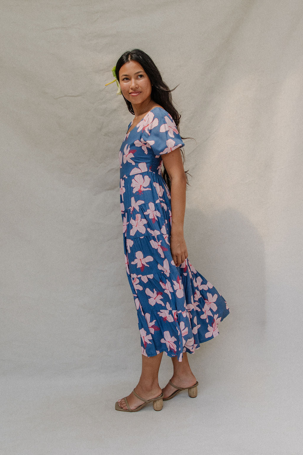 woman with brown hair wearing a navy scoop neck maxi dress with white hibiscus  print
