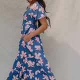 woman with brown hair wearing a navy scoop neck maxi dress with white hibiscus  print