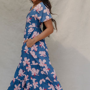 woman with brown hair wearing a navy scoop neck maxi dress with white hibiscus  print