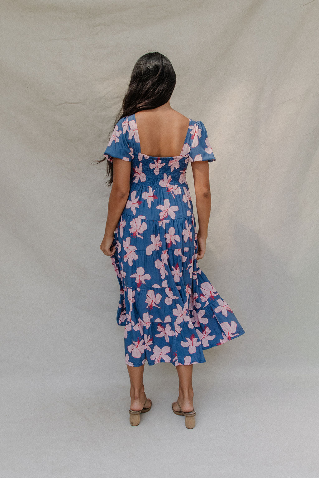 woman with brown hair wearing a navy scoop neck maxi dress with white hibiscus  print