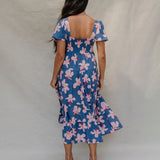woman with brown hair wearing a navy scoop neck maxi dress with white hibiscus  print