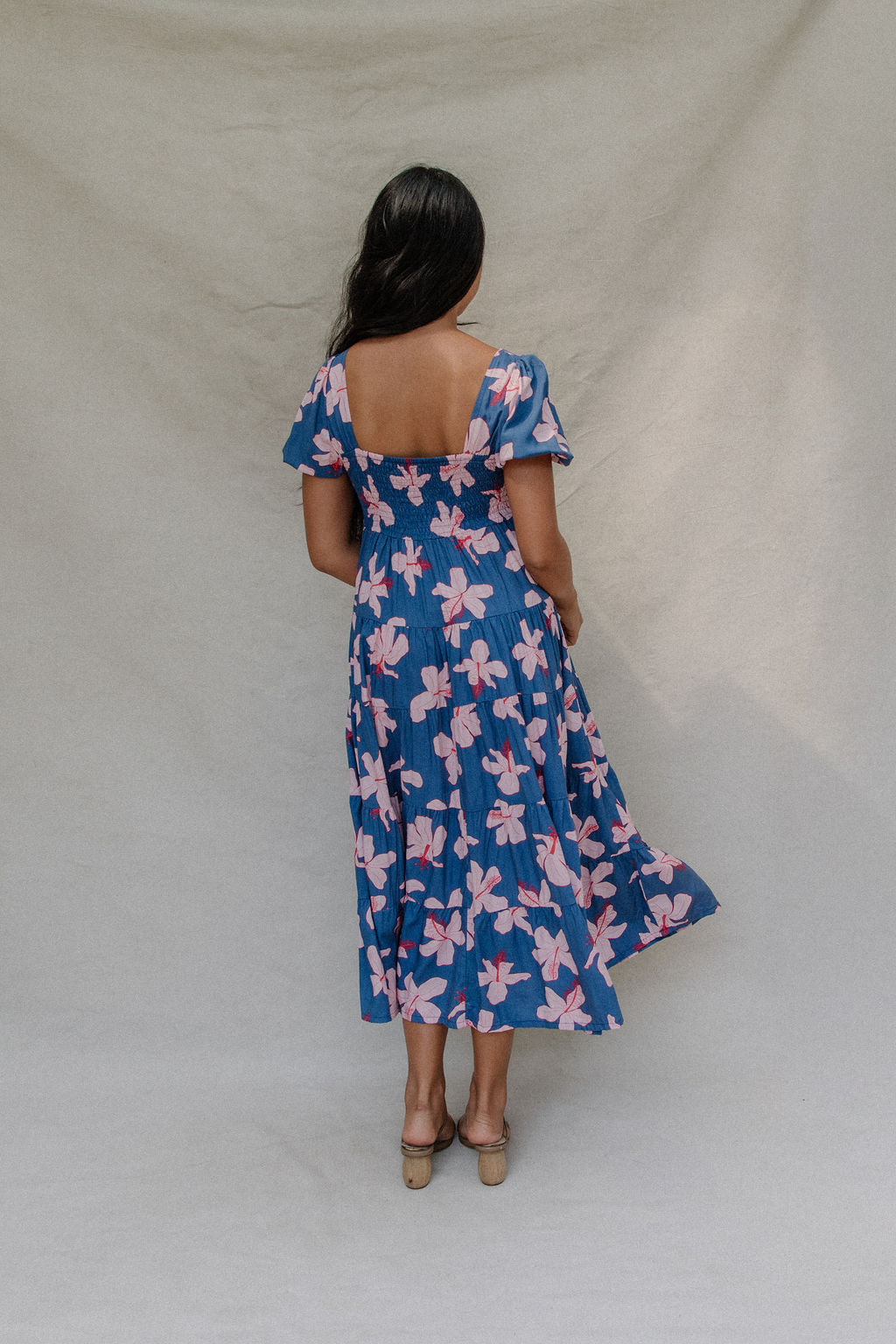 woman with brown hair wearing a navy scoop neck maxi dress with white hibiscus  print