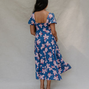 woman with brown hair wearing a navy scoop neck maxi dress with white hibiscus  print